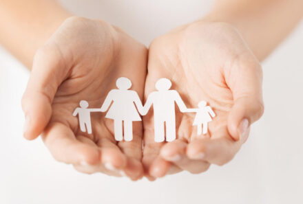 Hands holding a paper cut showing a family holding hands